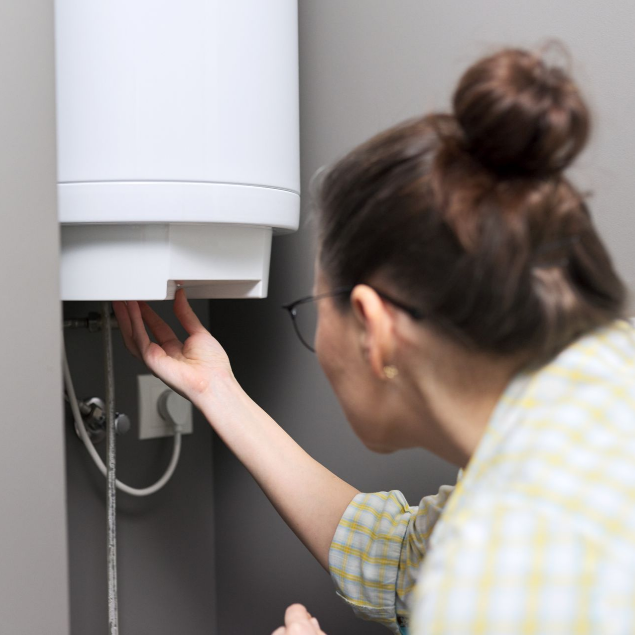 Une personne portant des lunettes examine un chauffe-eau blanc.
