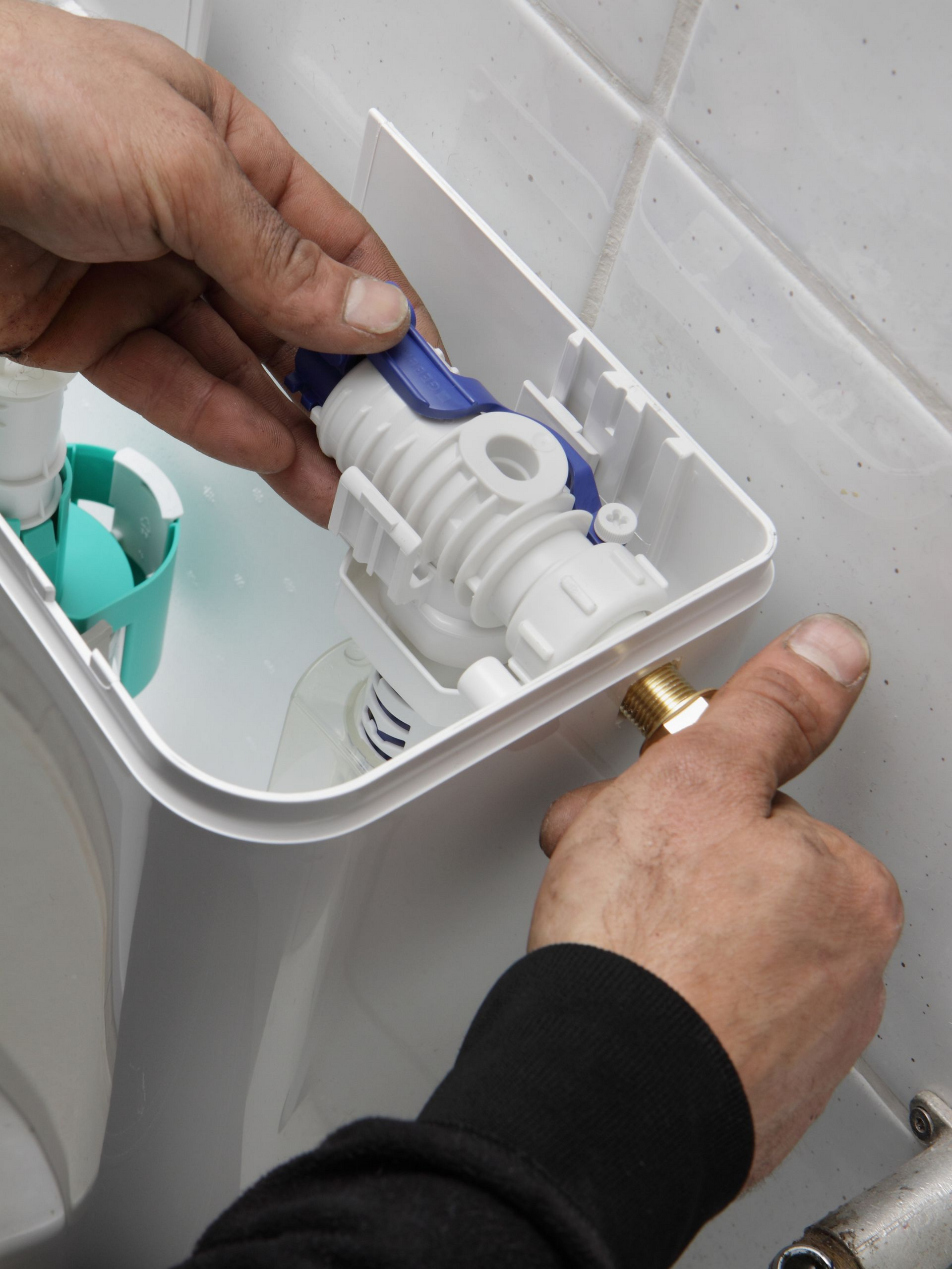 Des mains installent le mécanisme de chasse d'eau à l'intérieur d'un réservoir de toilettes.