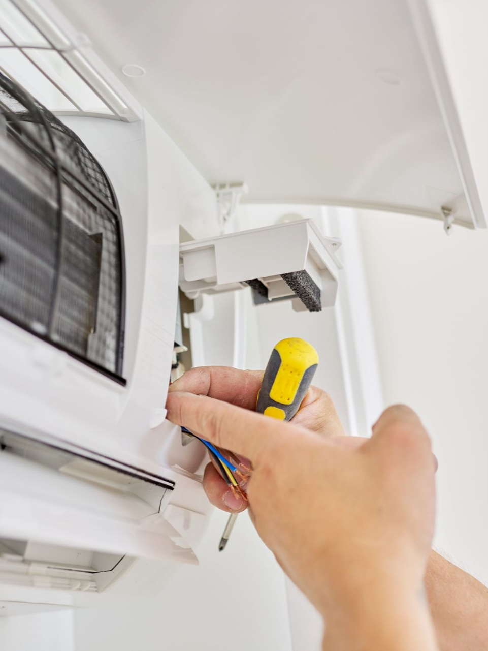 Une personne utilise un tournevis pour réparer un climatiseur mural.