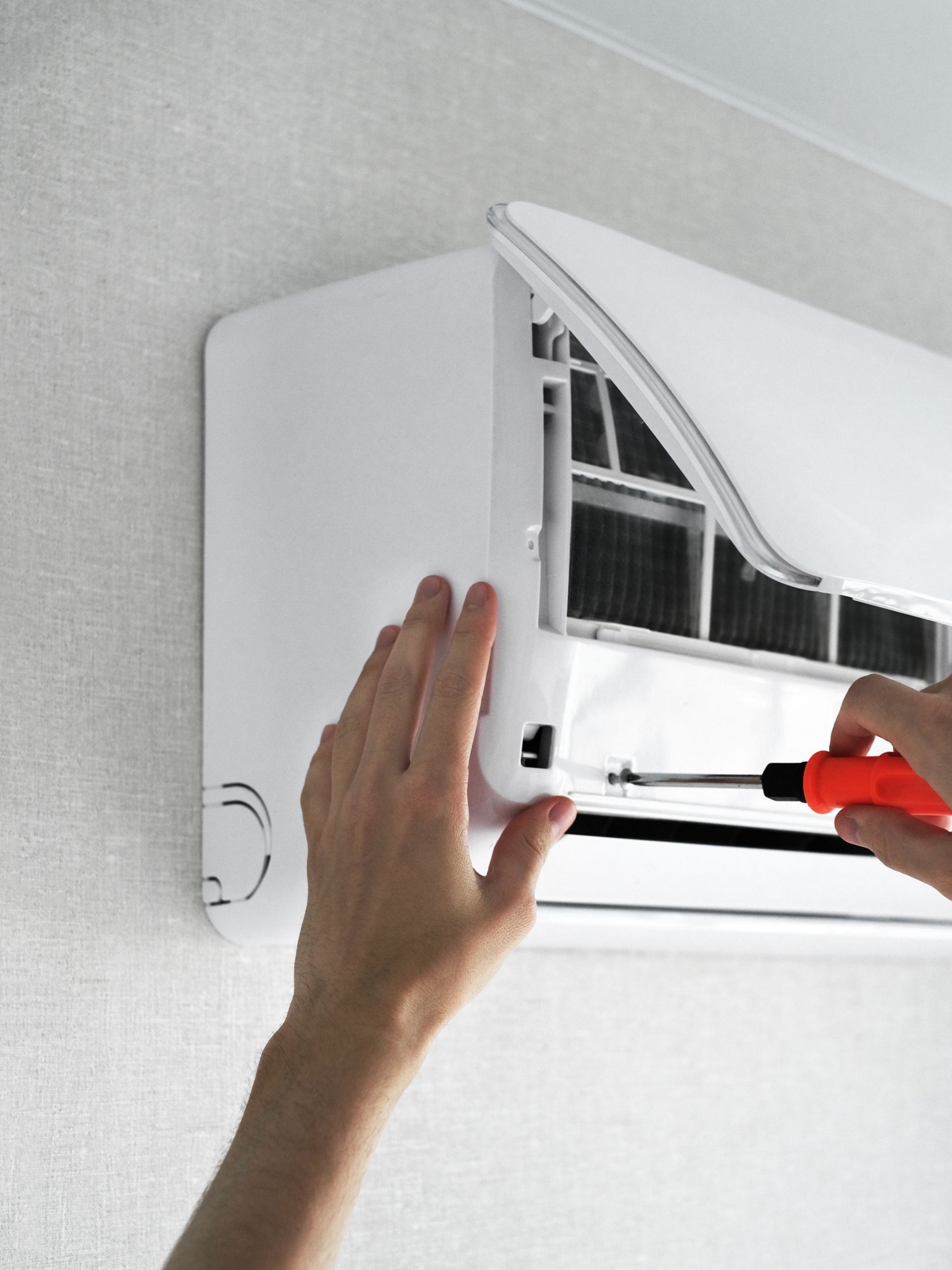 Une personne utilise un tournevis pour ouvrir un climatiseur pour l'entretien.