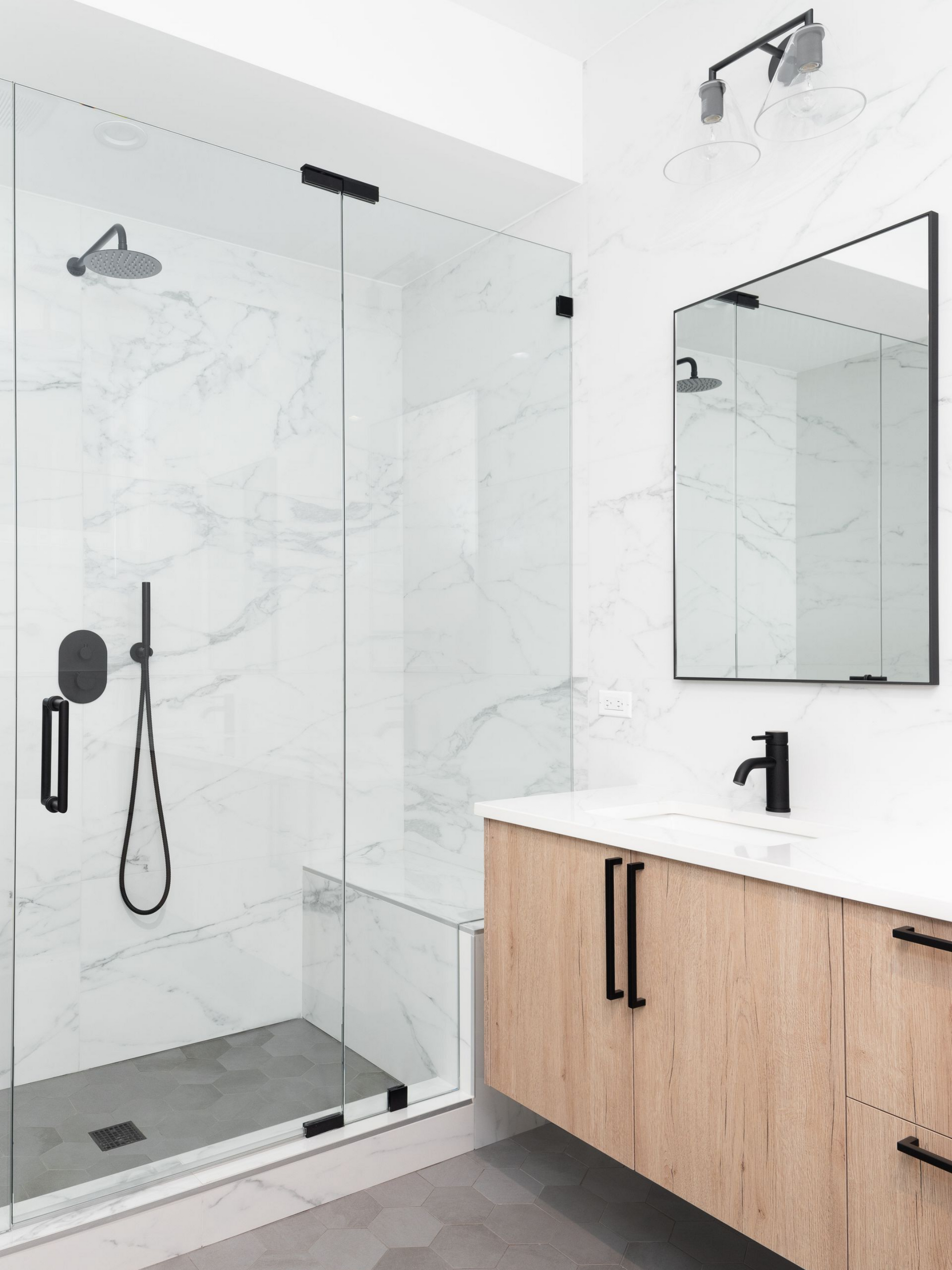 Salle de bains moderne avec murs en marbre, douche, meuble-vasque et robinetterie.