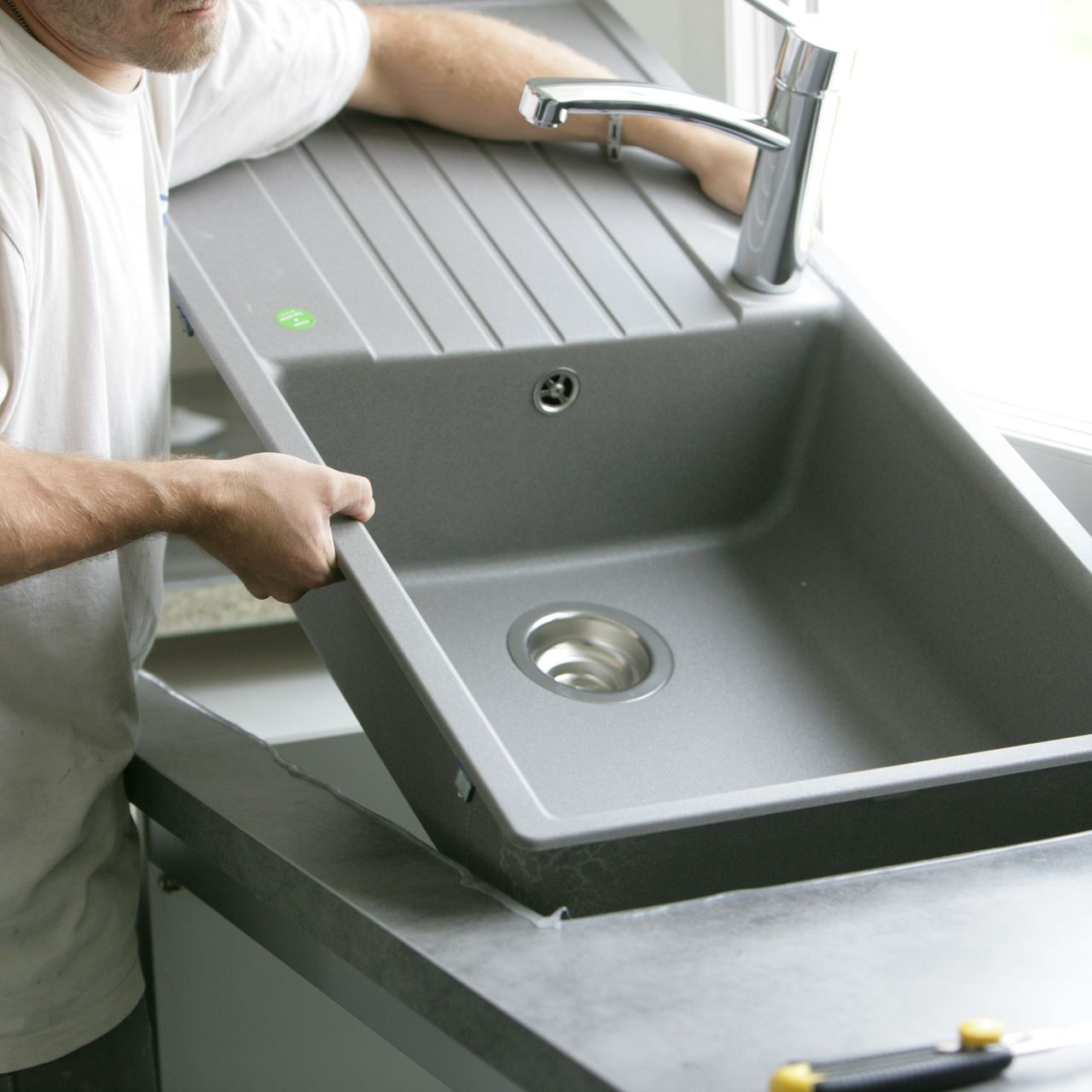 Personne installant un évier de cuisine gris.
