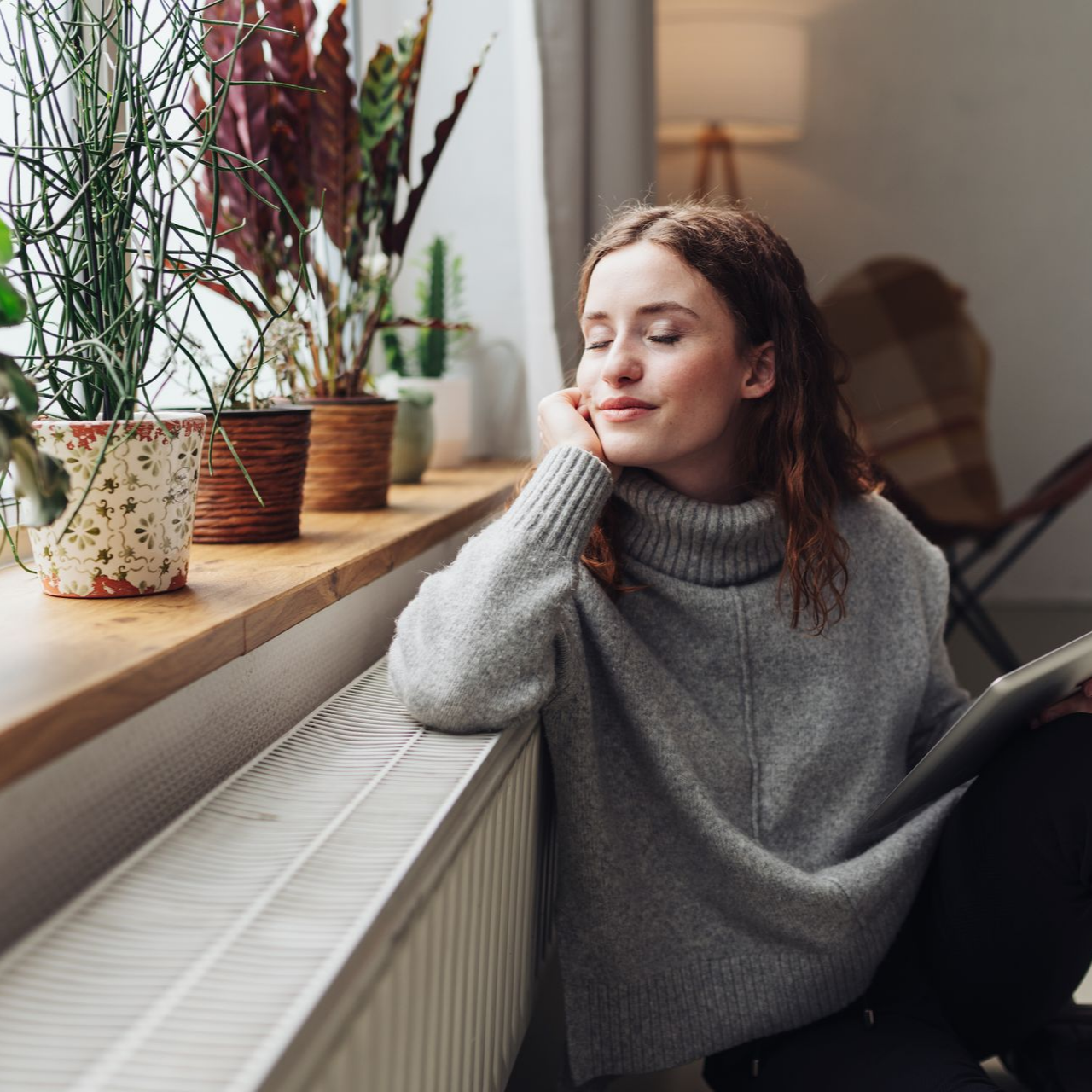 Femme qui a les yeux fermés, accoudée à un radiateur.