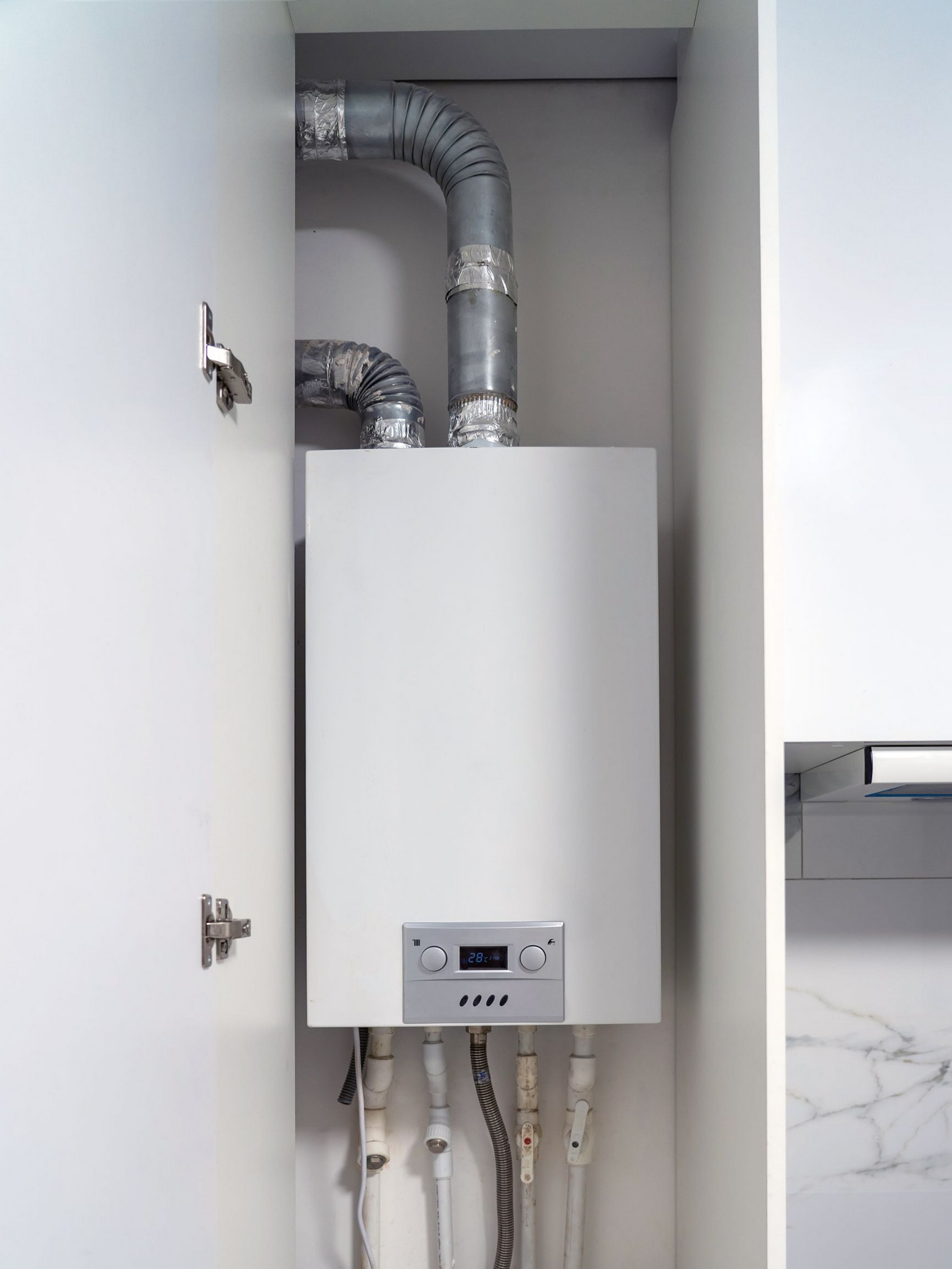Chaudière à gaz blanche installée dans un meuble blanc avec conduit d'évacuation au-dessus.