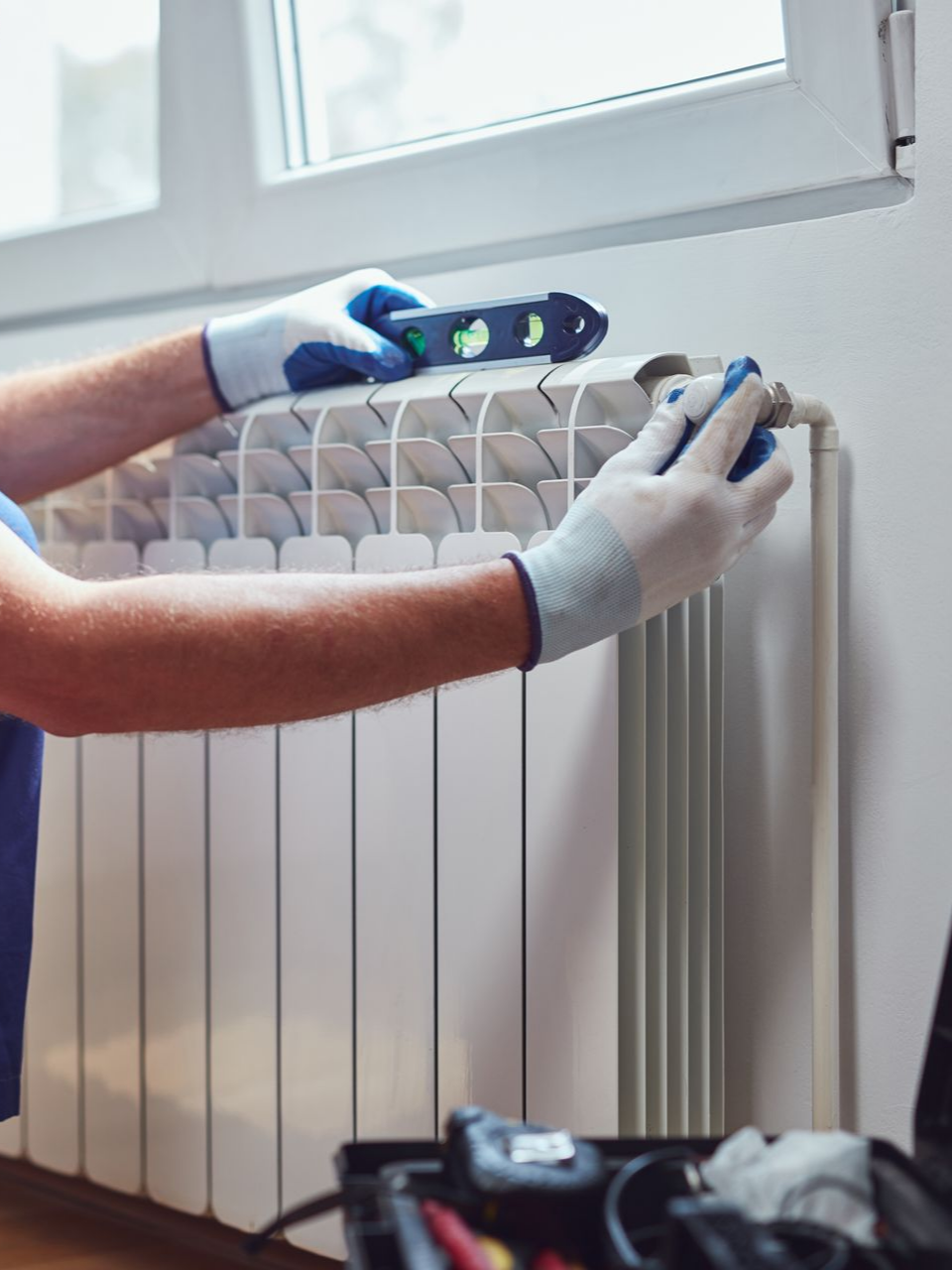 Une personne utilise un niveau sur un radiateur près d'une fenêtre.