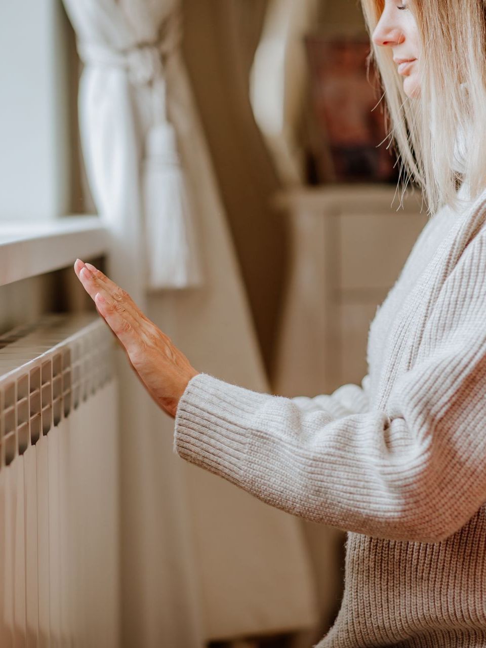 Une femme qui se réchauffe les mains devant un radiateur.