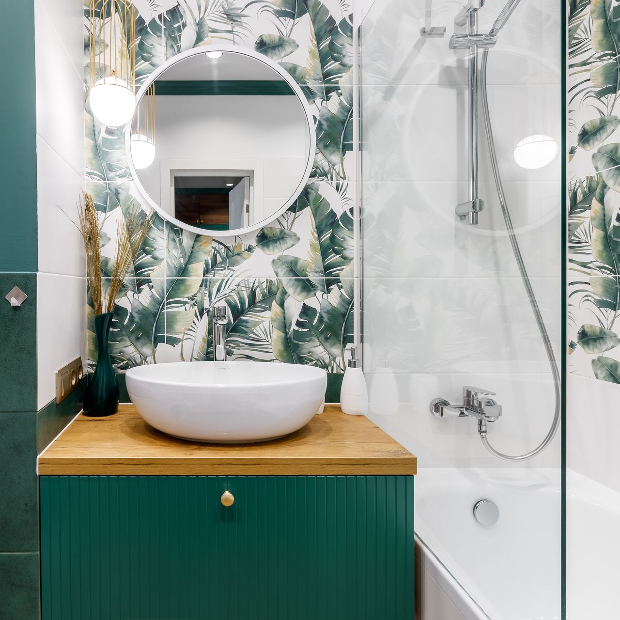 Salle de bains verte avec faïence tropicale, lavabo blanc, meuble en bois et douche.
