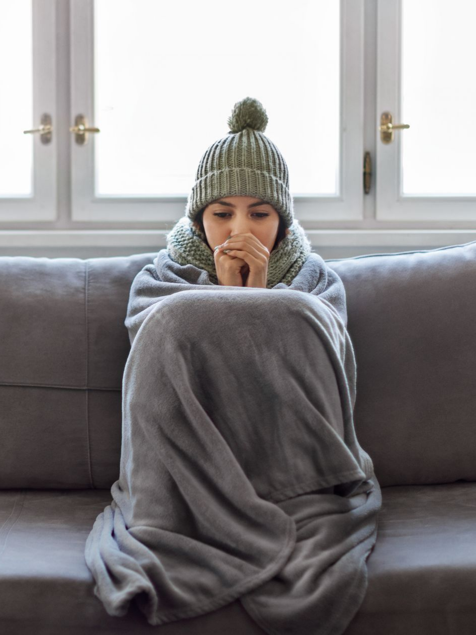 Une personne enveloppée dans une couverture, portant un bonnet, assise sur un canapé.