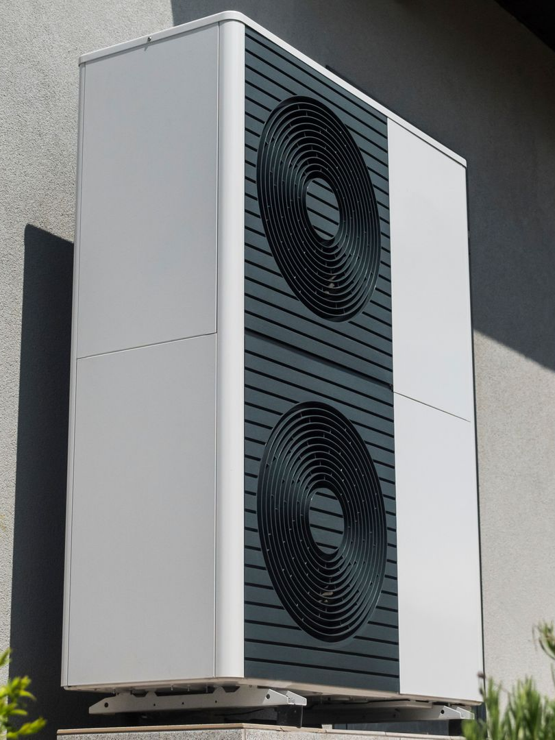 Pompe à chaleur blanche et grise fixée au mur, avec deux grilles de ventilation noires.