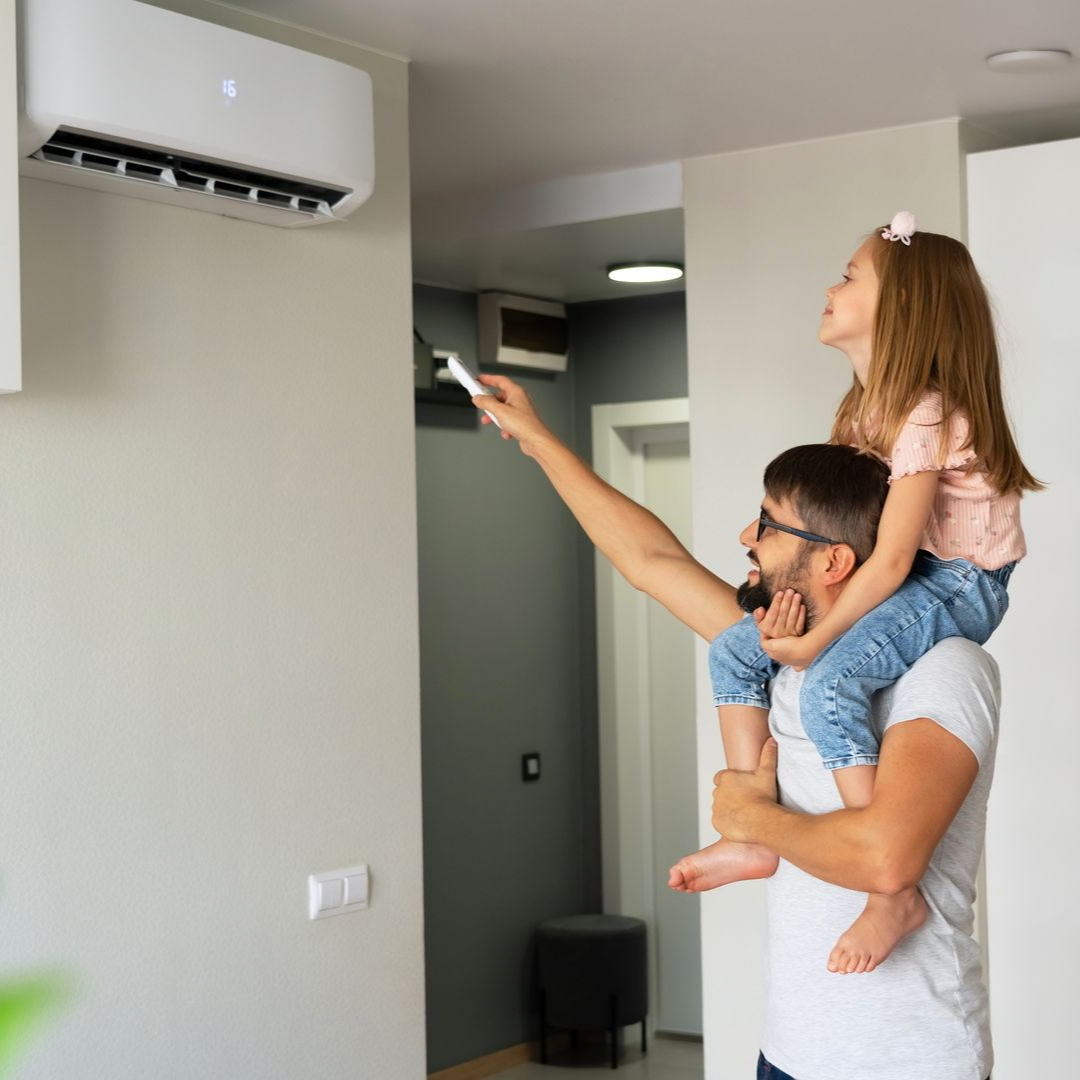Dans une pièce lumineuse, un homme portant un enfant sur ses épaules règle un climatiseur mural à l'aide d'une télécommande.