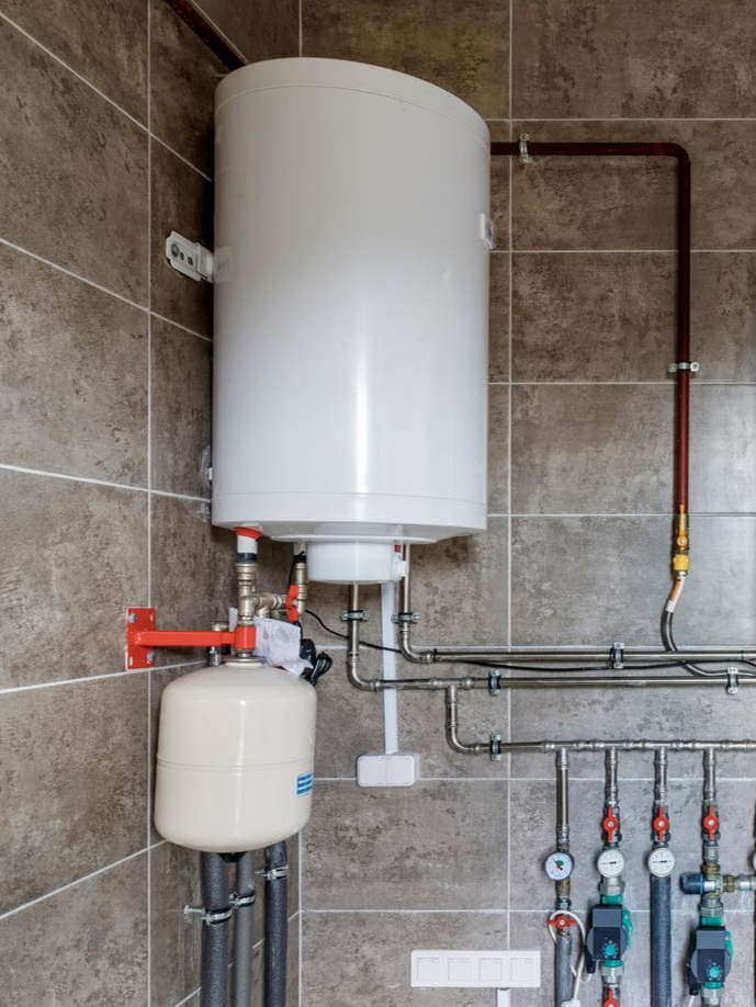 Chauffe-eau blanc et tuyauterie intégrée sur un mur carrelé.