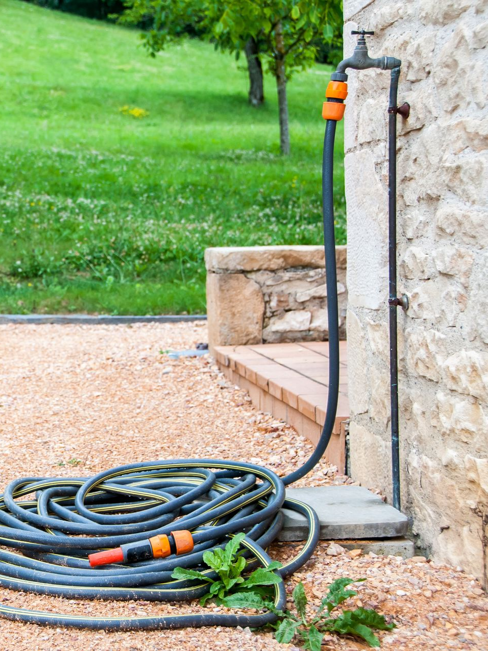 Un tuyau d'arrosage noir enroulé, raccordé à un robinet extérieur.