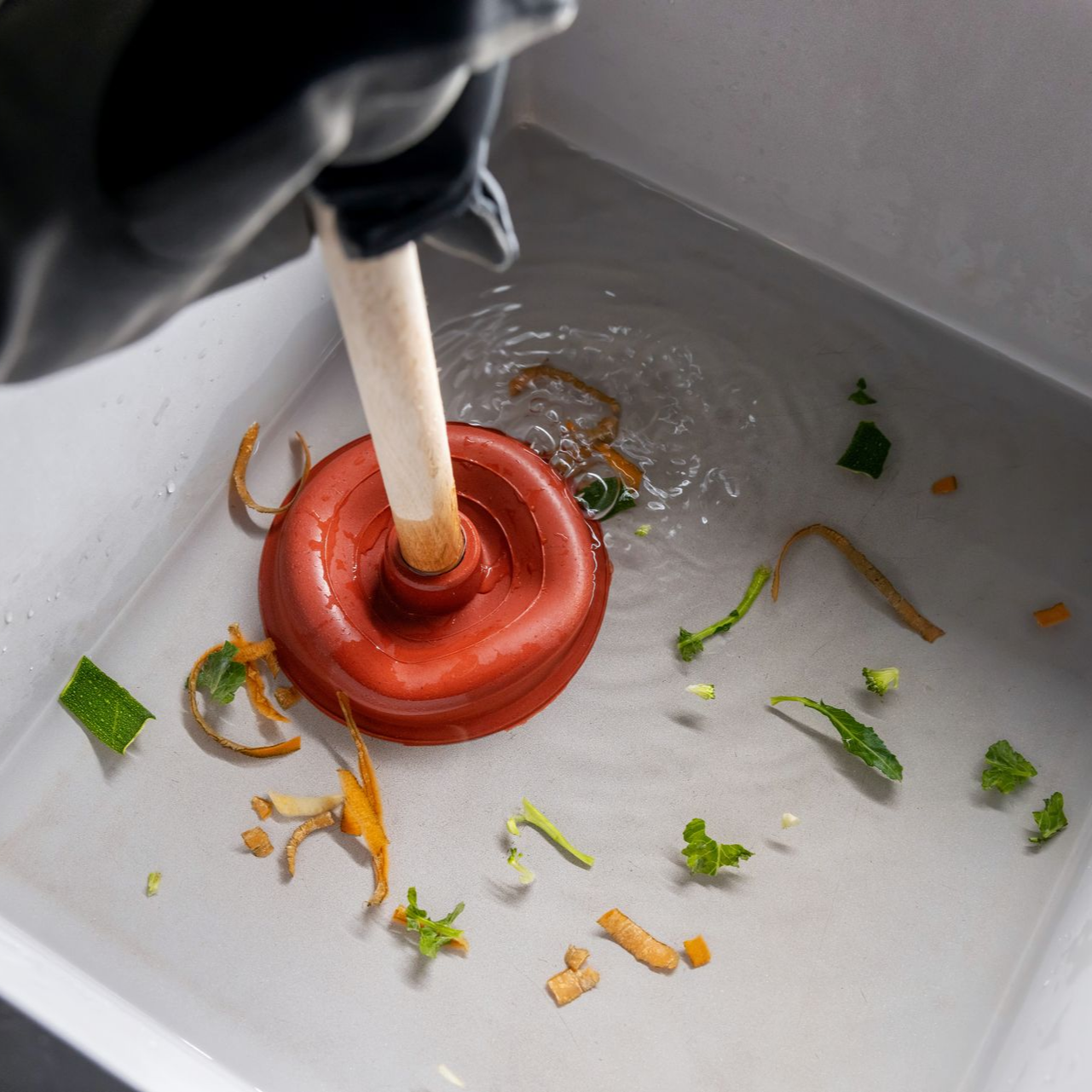 Une main gantée utilise une ventouse dans un évier rempli d'eau et de restes alimentaires.