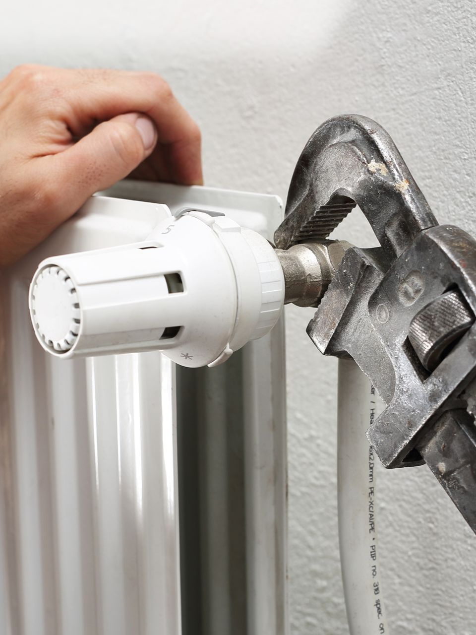 Personne utilisant une clé pour serrer un tuyau raccordé à une vanne de radiateur.