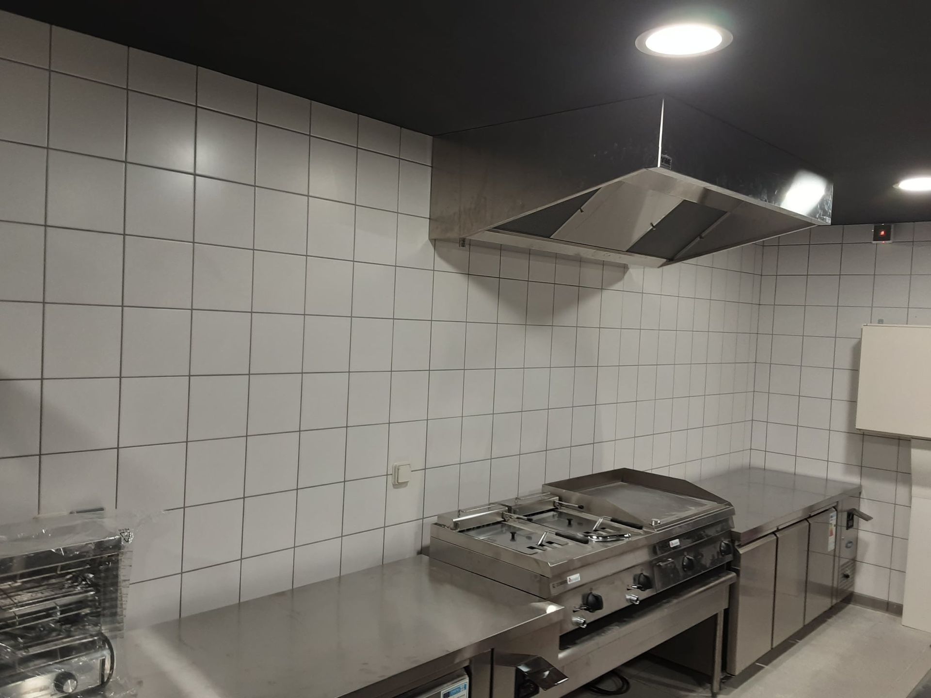 Cuisine en acier inoxydable avec cuisinière à gaz et hotte aspirante, murs carrelés blancs.