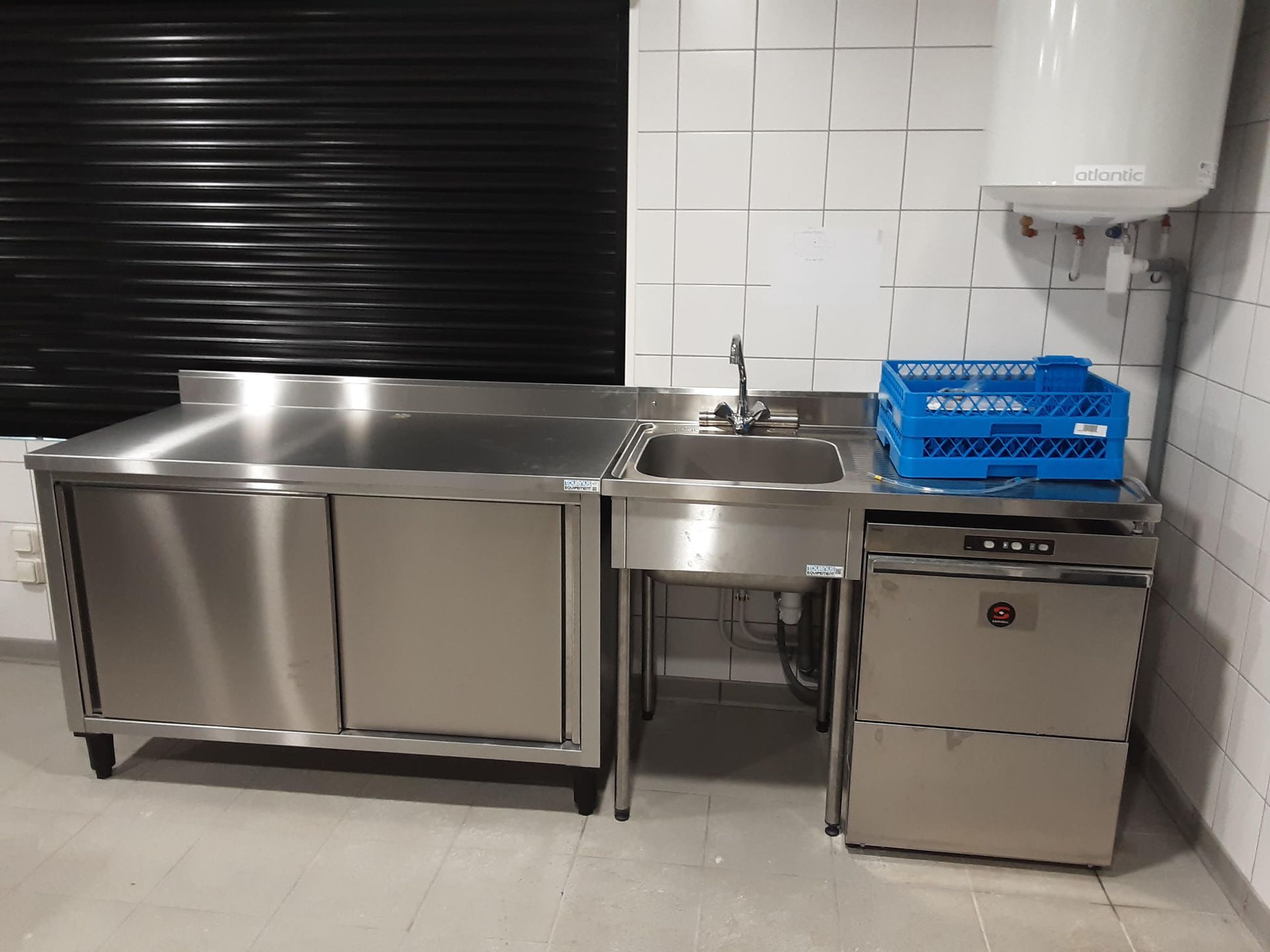 Évier et lave-vaisselle de cuisine professionnels en acier inoxydable. Égouttoir à vaisselle bleu sur le dessus. Store noir.