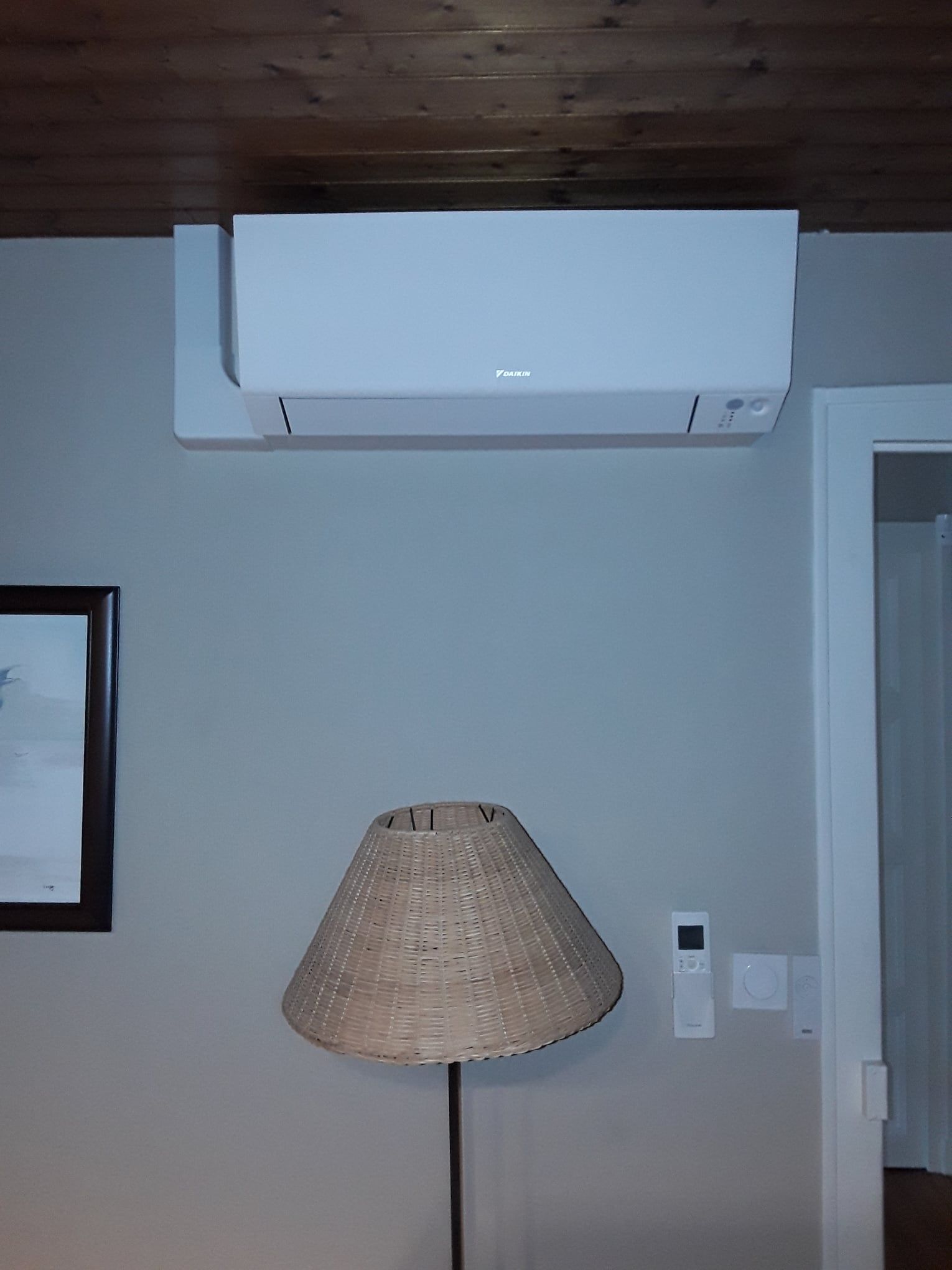 Unité de climatisation blanche fixée sur un mur gris au-dessus d'une lampe. Plafond en bois.