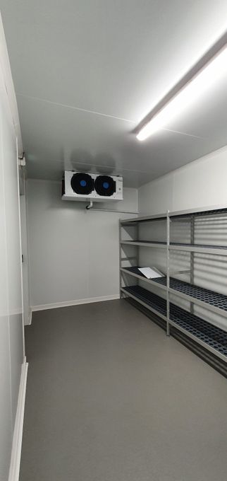 Intérieur d'une chambre froide, avec des étagères à droite et un climatiseur au plafond.