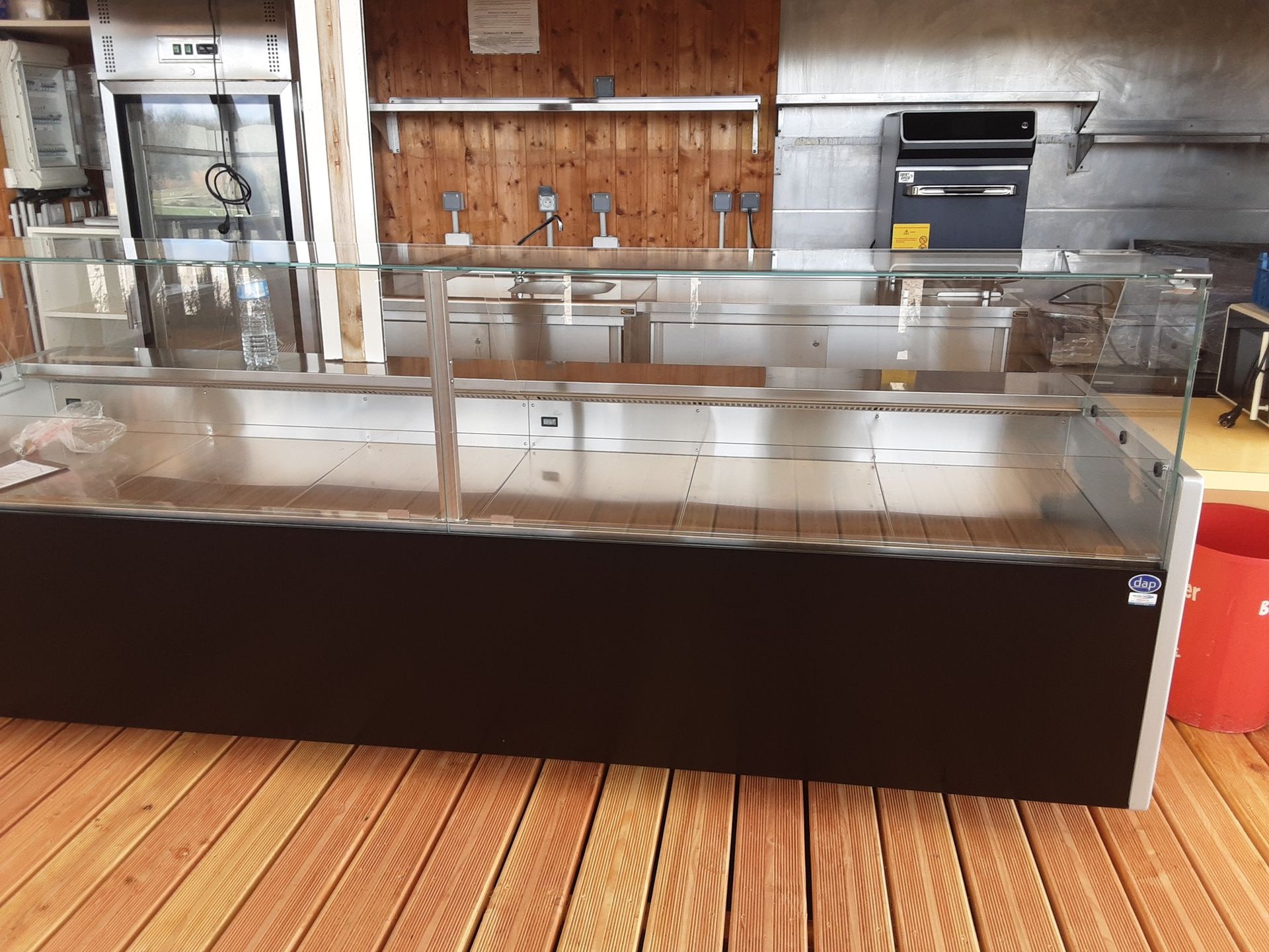 Vitrine réfrigérée vide dans un environnement commercial ; sol et mur en bois.