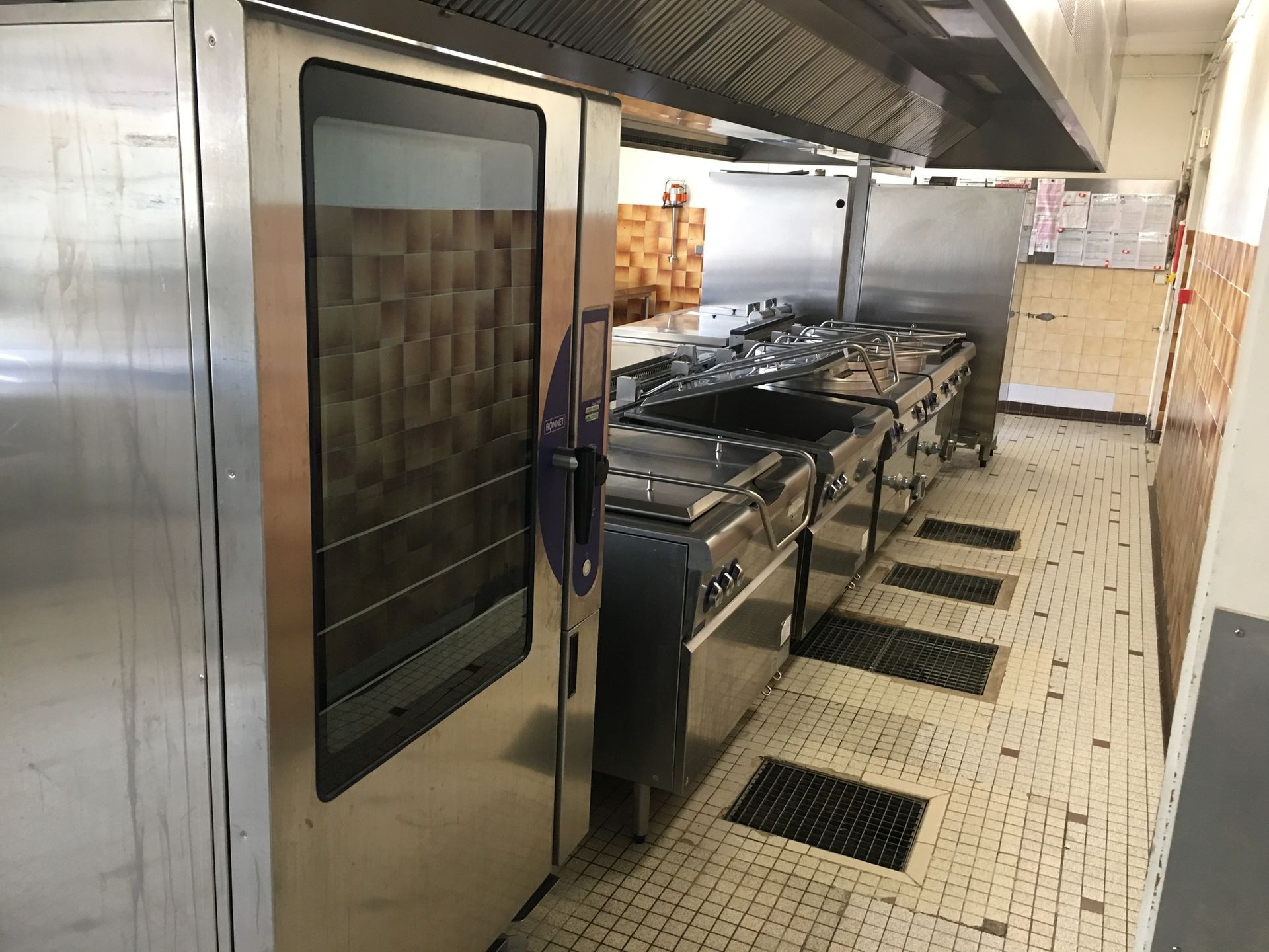 Cuisine commerciale équipée d'appareils en acier inoxydable, four, cuisinière et siphon de sol.