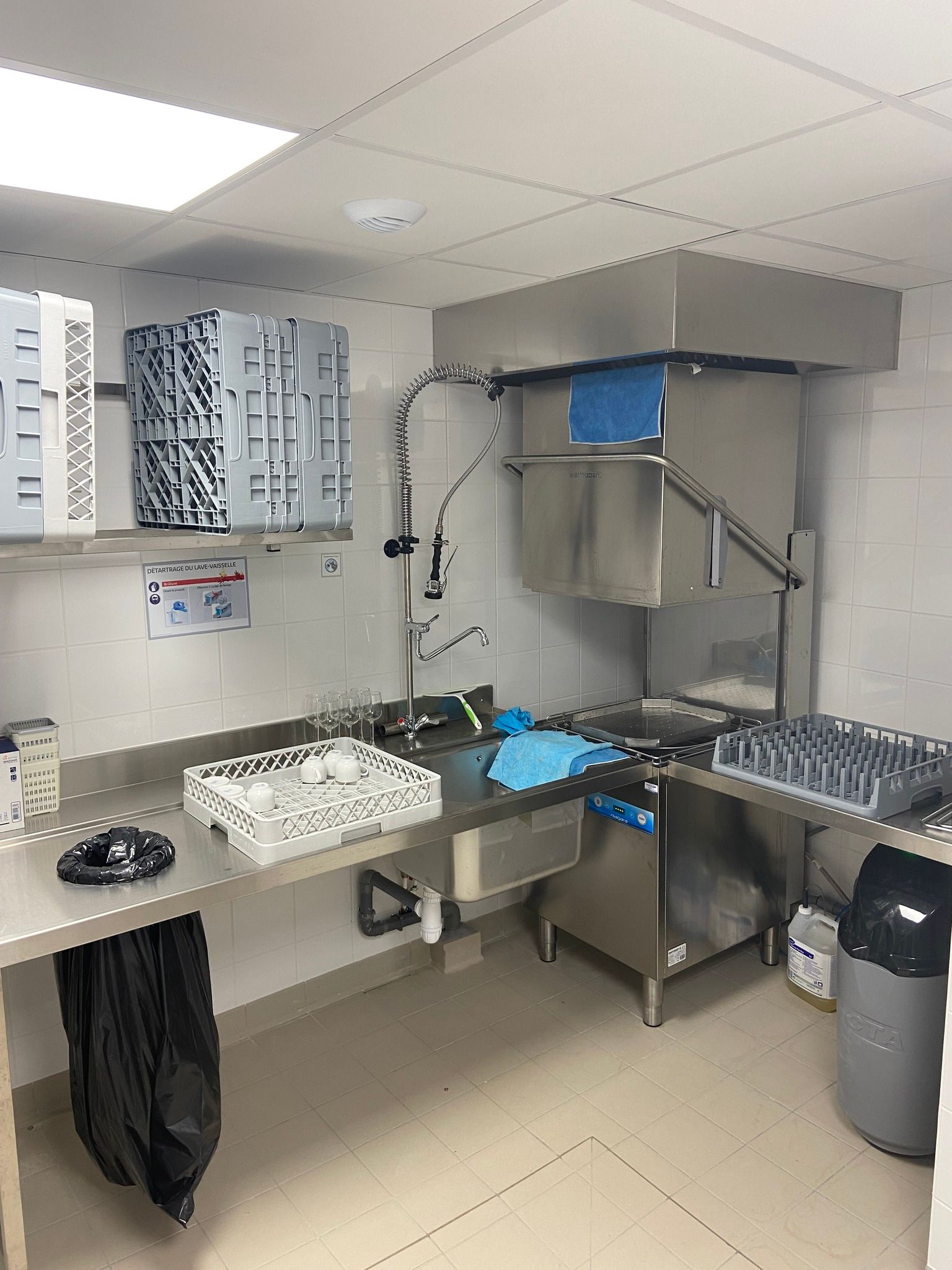 Cuisine professionnelle équipée d'un grand lave-vaisselle, de surfaces en acier inoxydable et d'une poubelle.