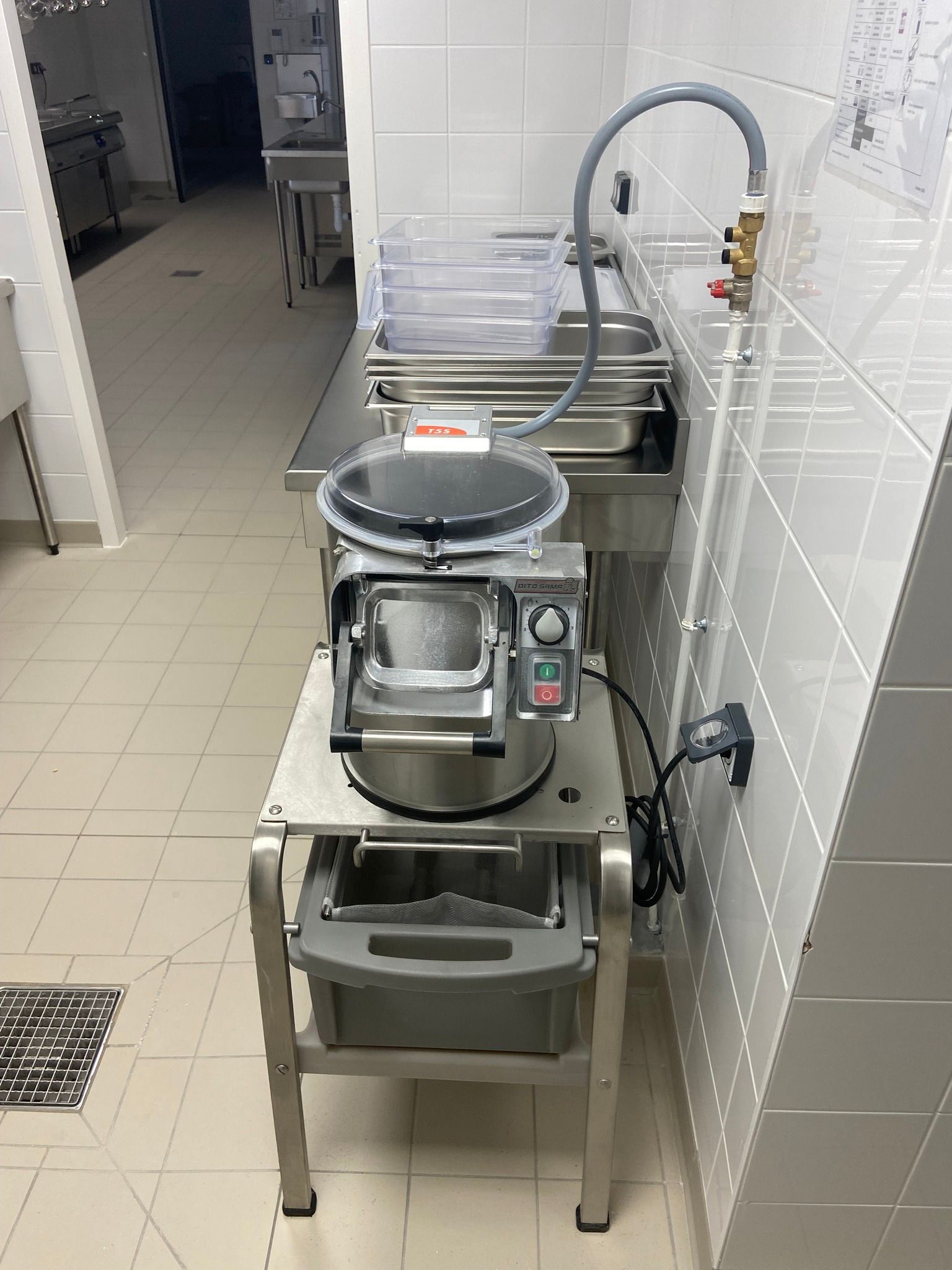 Cuisine professionnelle : robot culinaire sur support métallique, avec tuyau d’arrosage et système d’évacuation.