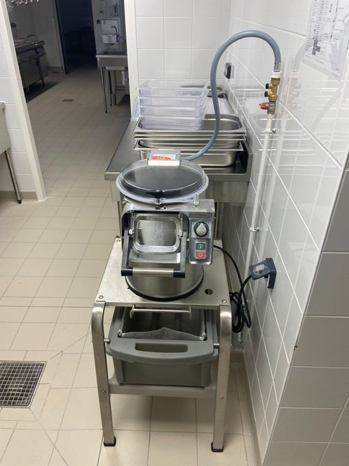 Cuisine professionnelle : robot culinaire sur support métallique, avec tuyau d’arrosage et système d’évacuation.