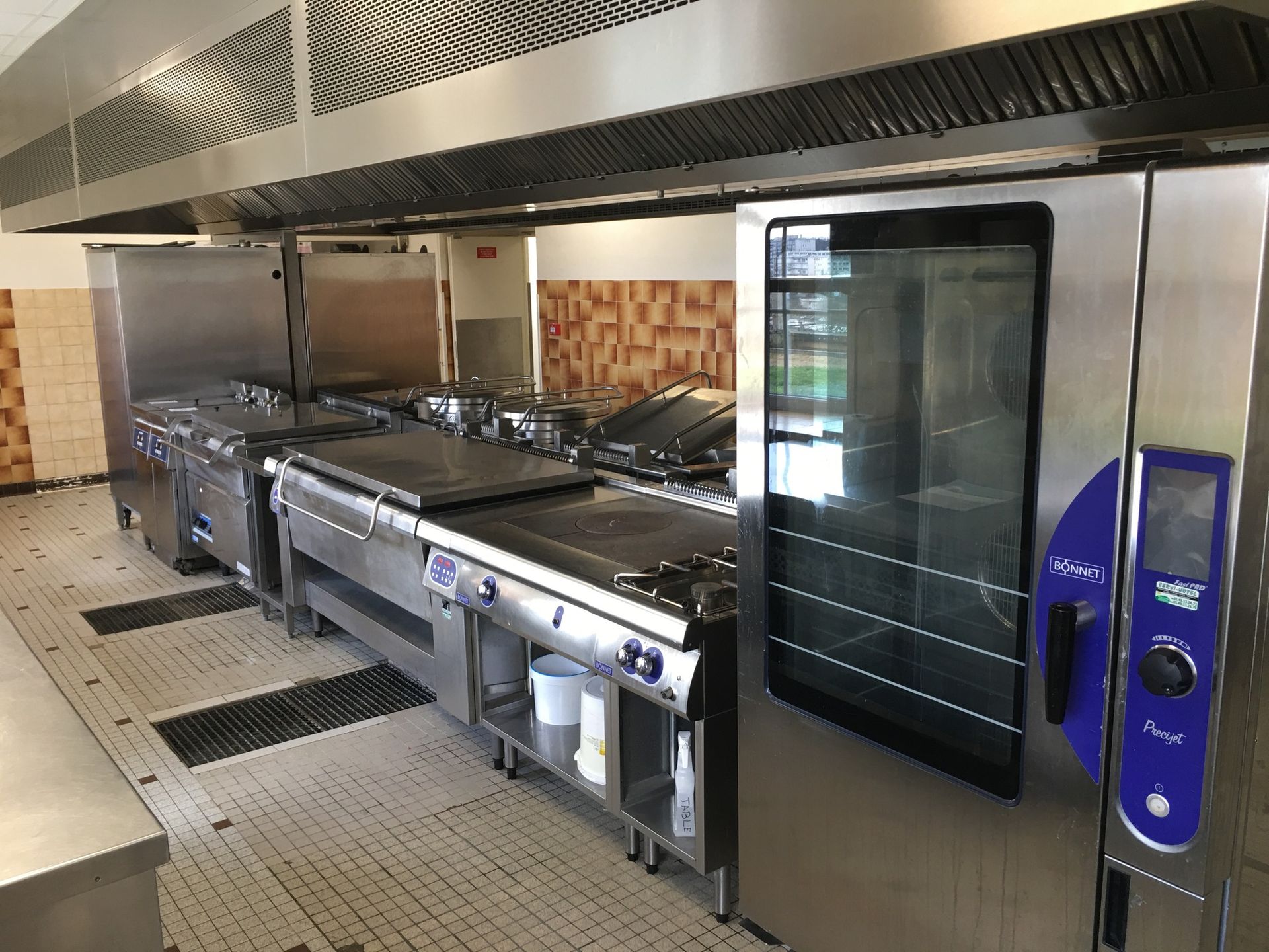 Cuisine commerciale équipée d'appareils en acier inoxydable, comprenant four, plaques de cuisson et plaque de cuisson, sous une hotte aspirante.