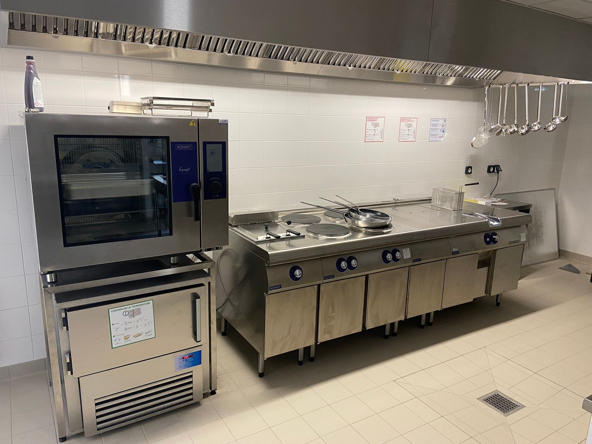 Cuisine commerciale équipée d'appareils en acier inoxydable, comprenant un four, une cuisinière et un réfrigérateur.