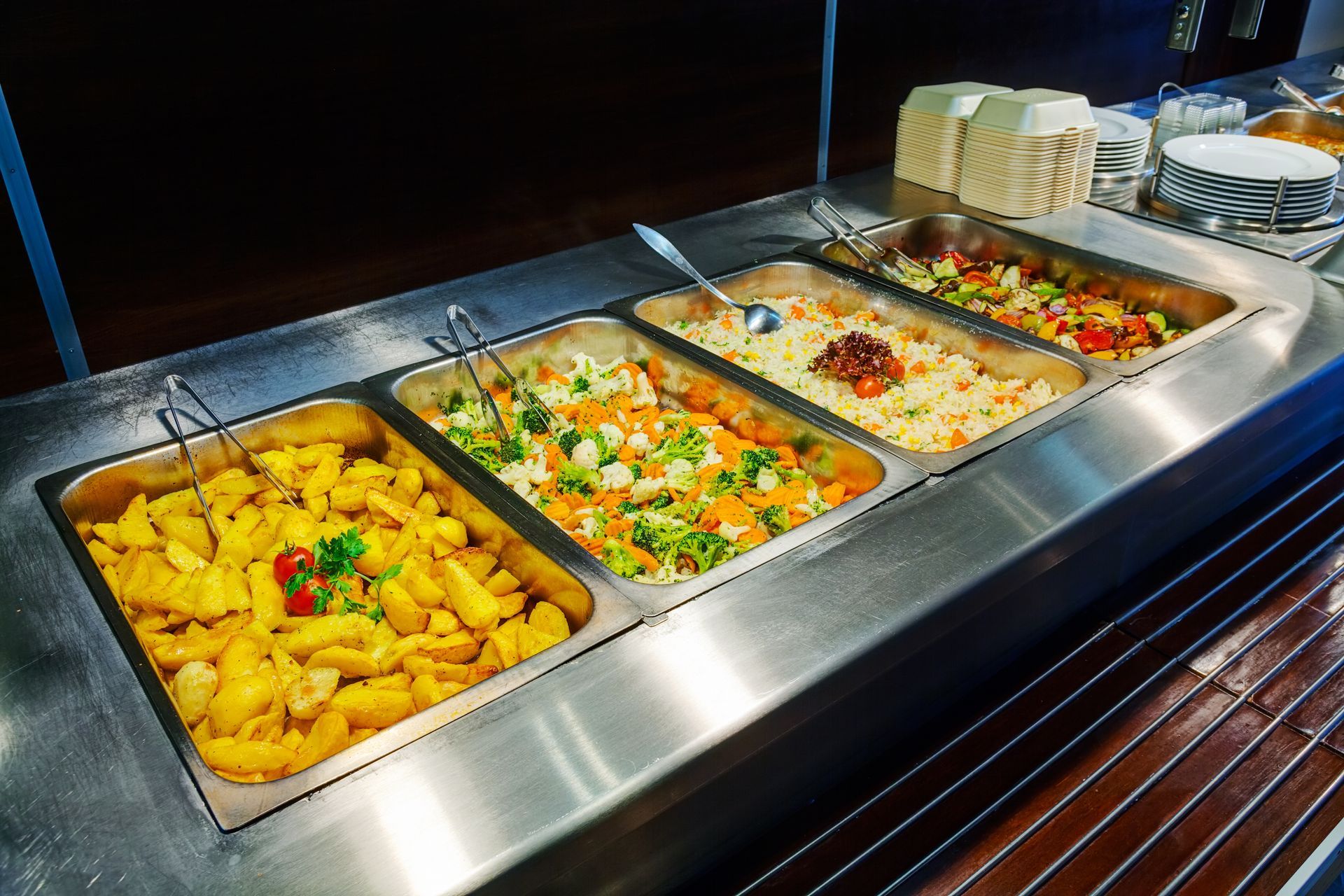 Buffet composé de quatre plateaux : pommes de terre, légumes variés, riz et salade.