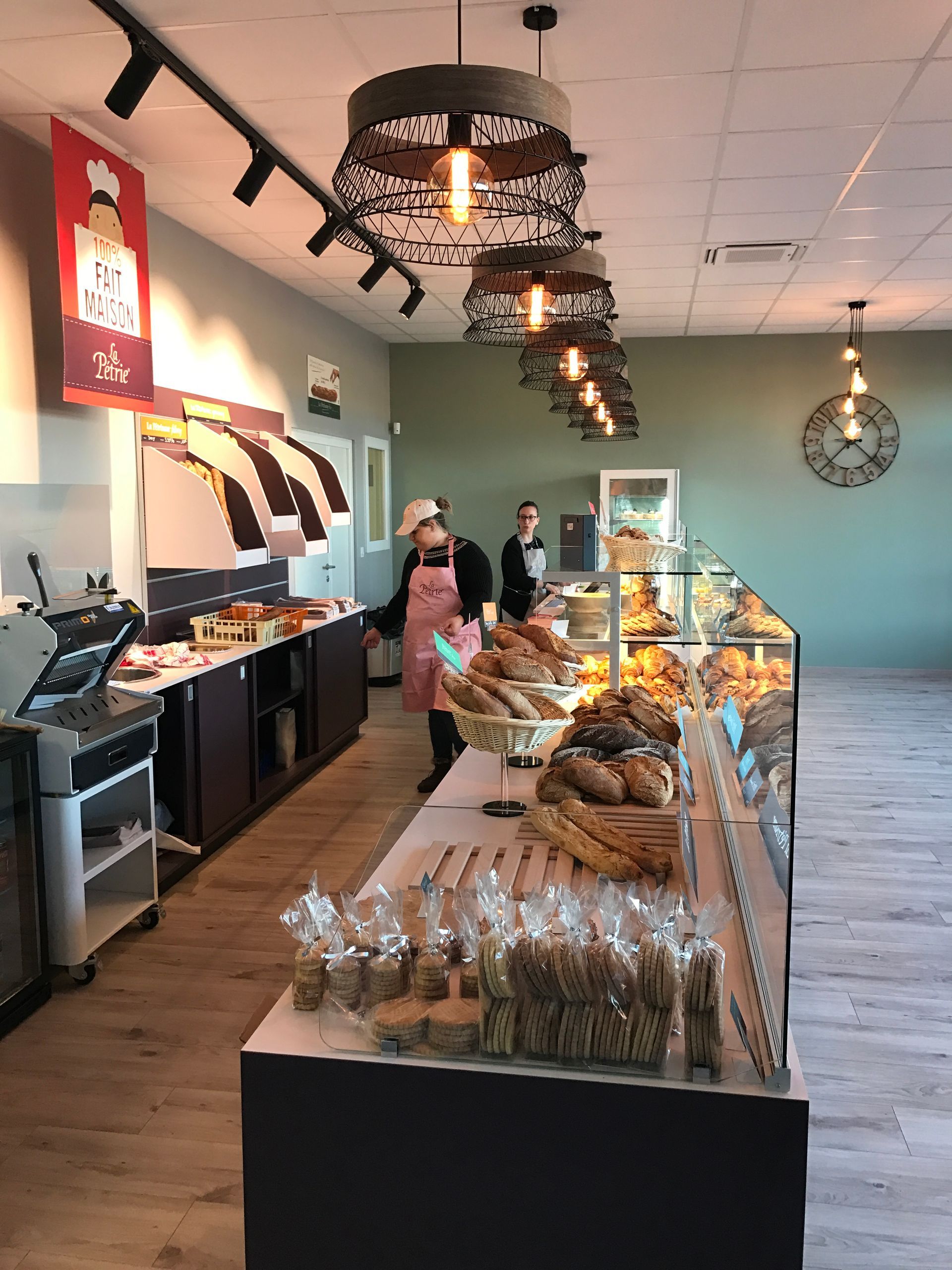 Intérieur d'une boulangerie avec des produits de boulangerie exposés ; personnel derrière le comptoir, éclairage zénithal.