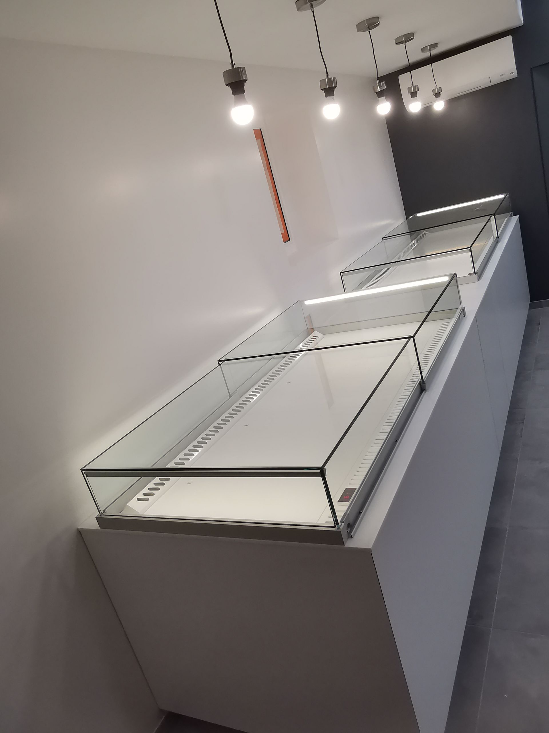 Vitrines à plateau en verre et socle blanc, éclairées par le haut, dans un magasin.