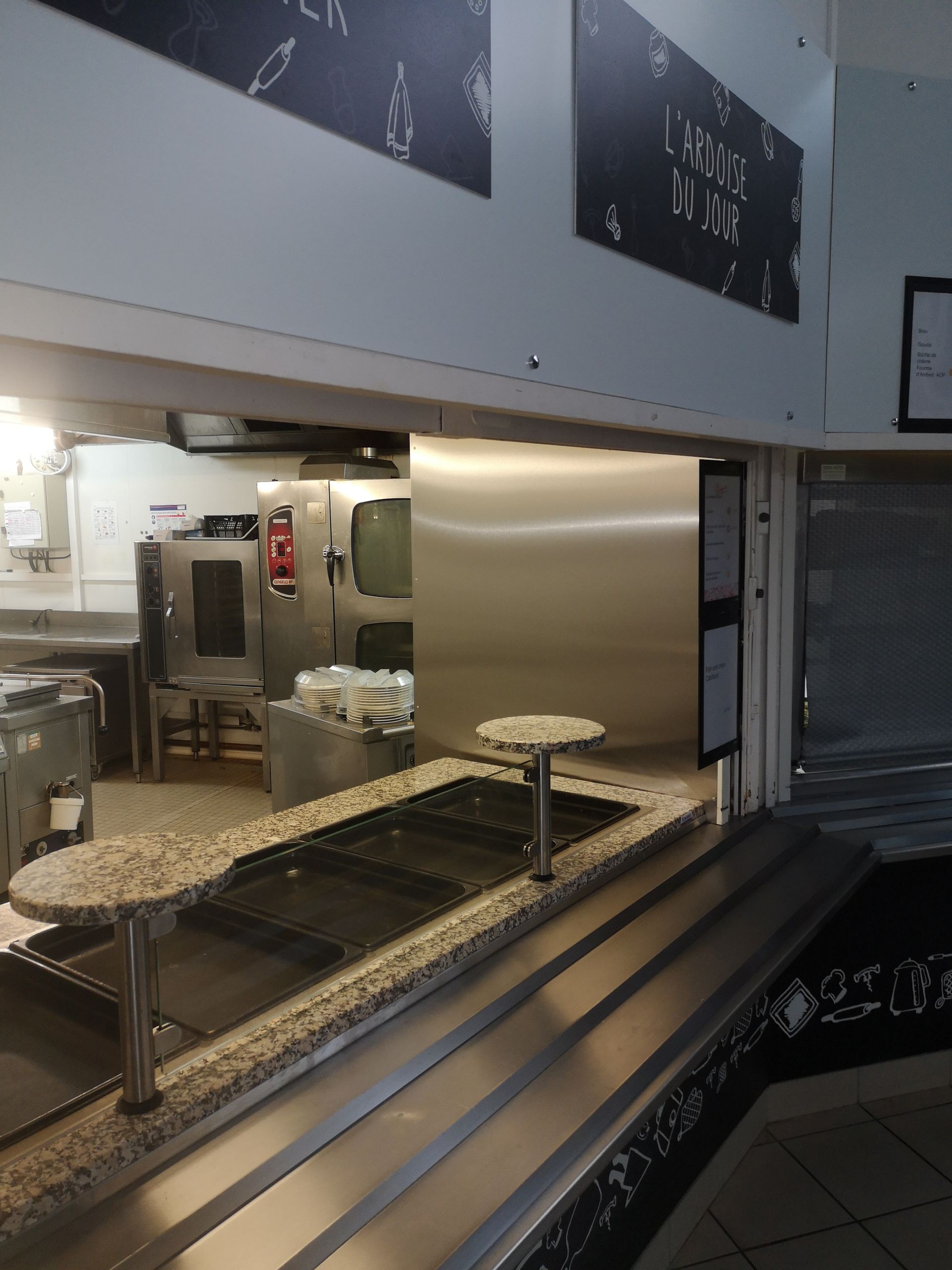 Comptoir de cuisine de restaurant, en acier inoxydable, avec deux tables rondes et un plateau en granit, donnant sur les équipements de cuisson.