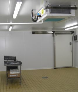 Une chambre froide aux murs blancs, avec une porte coulissante, un éclairage zénithal et un système de climatisation.