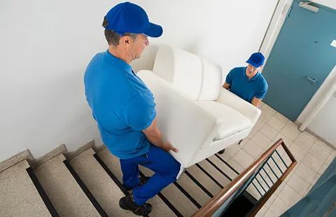 Dos repartidores suben un sofá blanco por unas escaleras.