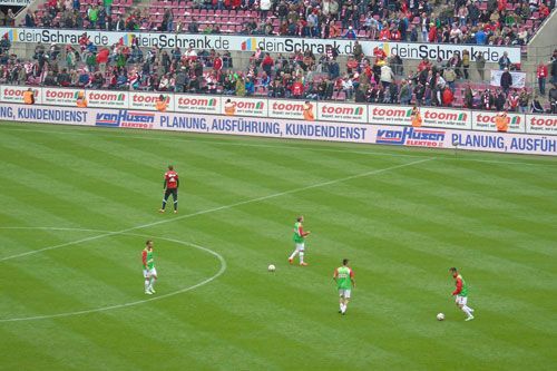 Eine Gruppe Fußballspieler spielt auf einem Feld vor Publikum.