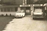 Ein Schwarzweißfoto von zwei vor einem Gebäude geparkten Autos.