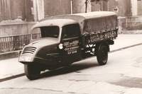 Ein Schwarzweißfoto eines dreirädrigen Lastwagens, der eine Straße entlangfährt.