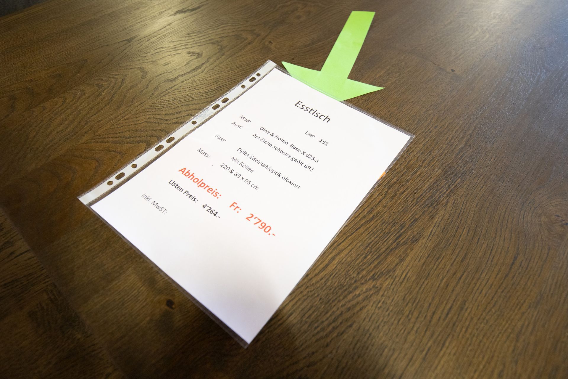 Auf einem Holztisch liegt ein Blatt Papier mit einem nach unten zeigenden Pfeil.