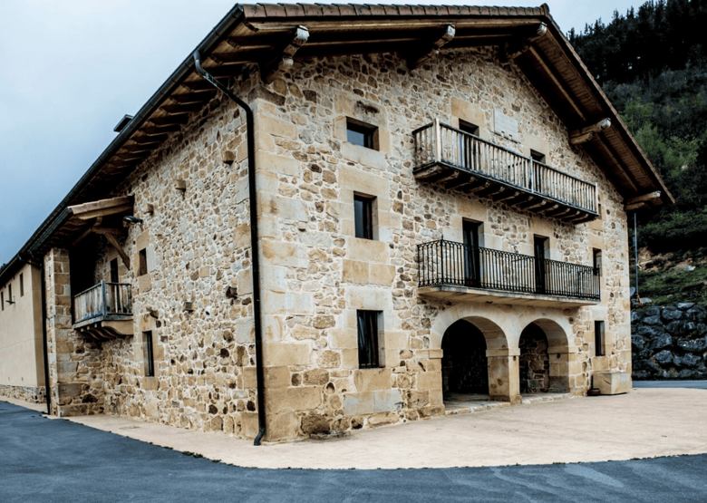 Edificio de piedra con entrada arqueada y balcones bajo cubierta inclinada, en un entorno de montaña.