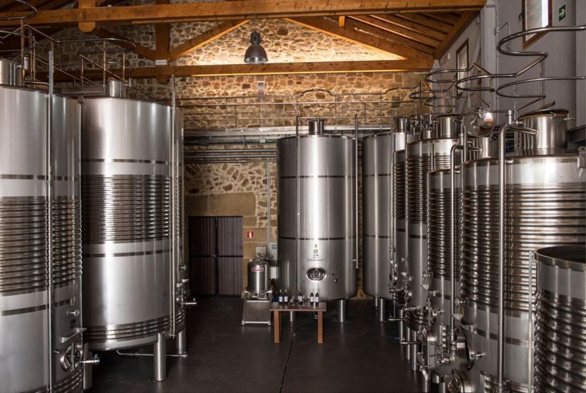 Tanques de vino de acero inoxidable en una bodega. Filas de contenedores cilíndricos en un edificio con paredes de piedra.