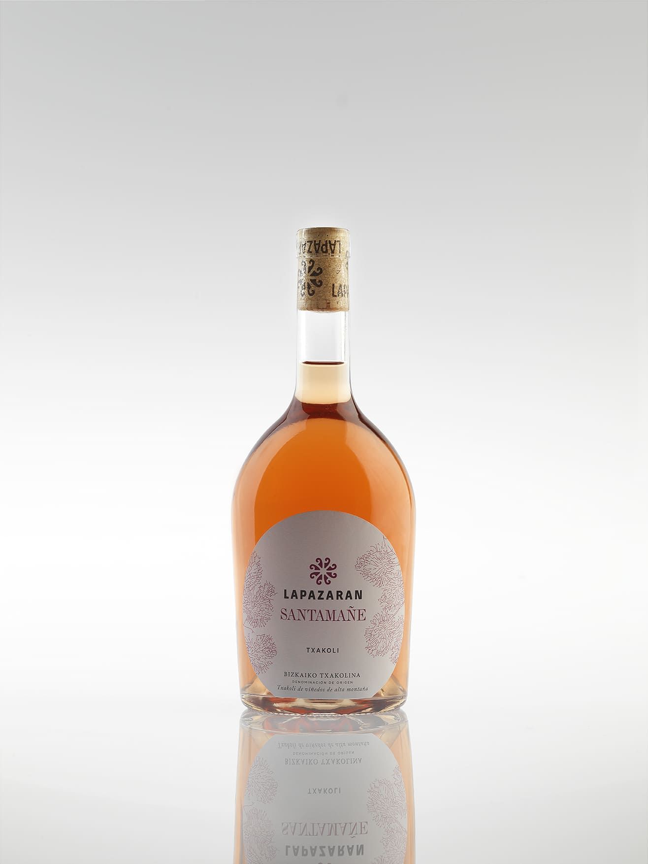 Botella de vino rosado, etiqueta visible, líquido rosa pálido, sobre fondo blanco.