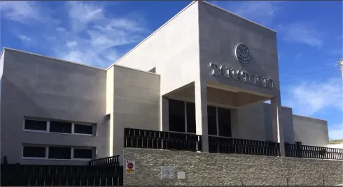 Edificio de hormigón blanco con ventanas, entrada y balcón oscuros, cielo soleado.