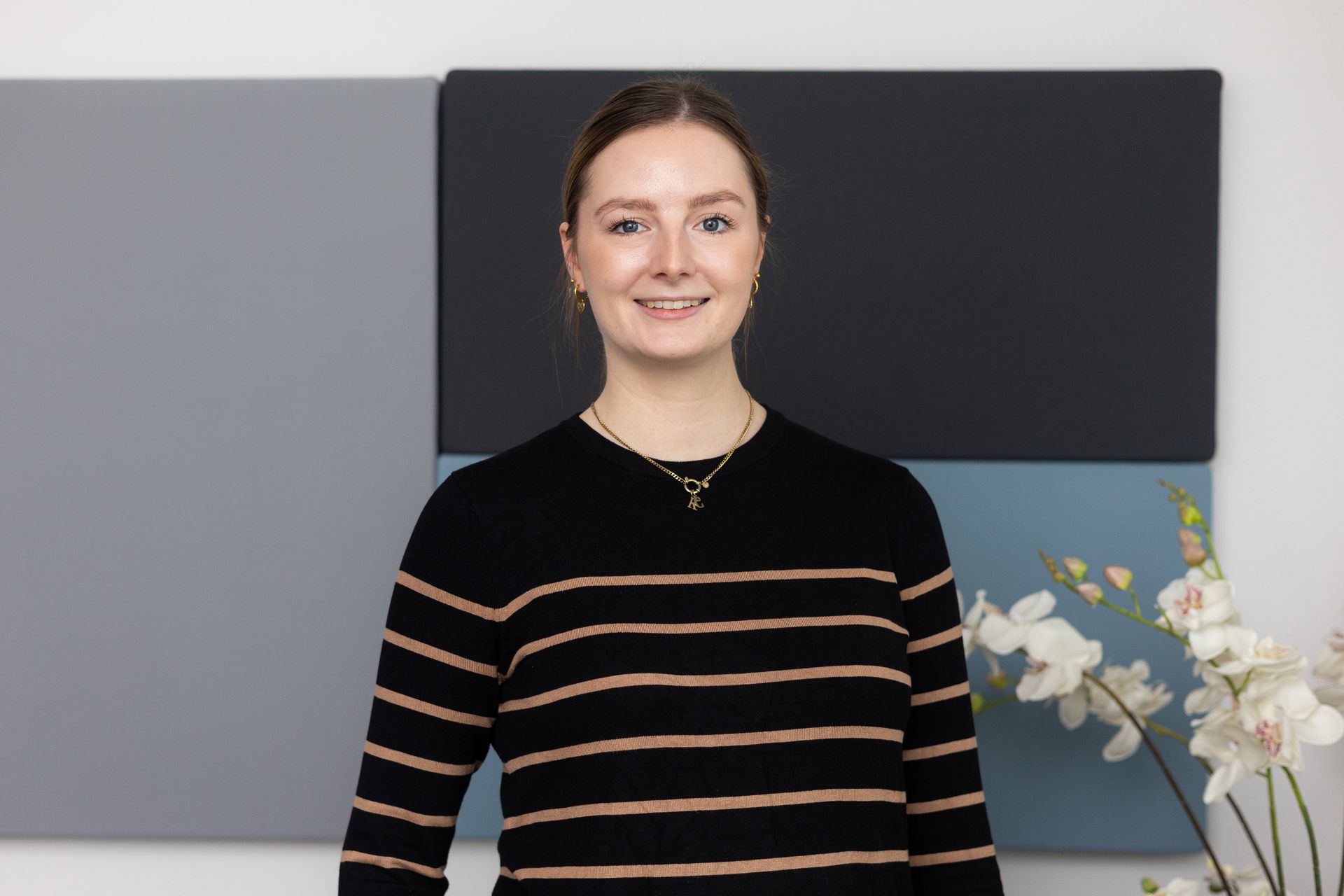 Person mit braun-schwarz gestreiftem Pullover und goldener Halskette.