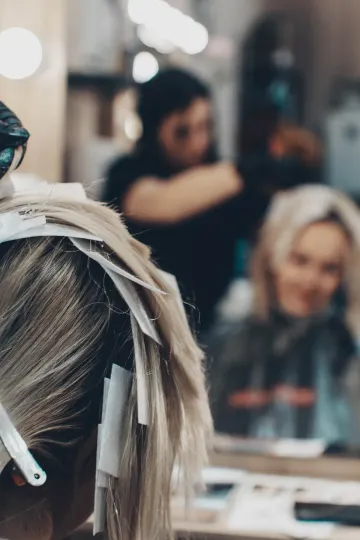 Cabello rubio con mechones de papel en el salón. Estilista detrás de una clienta, trabajando en el cabello.