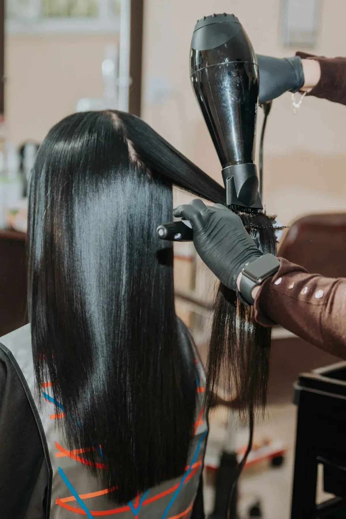 Estilista secando y alisando cabello largo y oscuro en un salón.