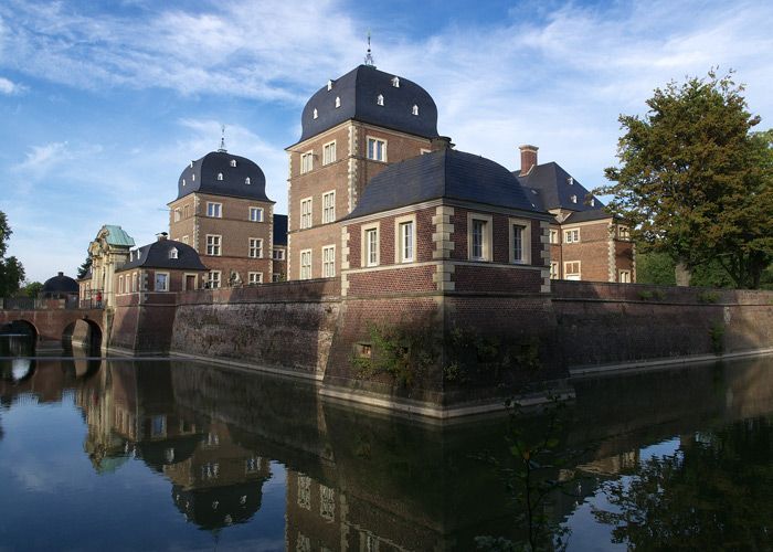 Ein großes Backsteingebäude spiegelt sich in einem Gewässer