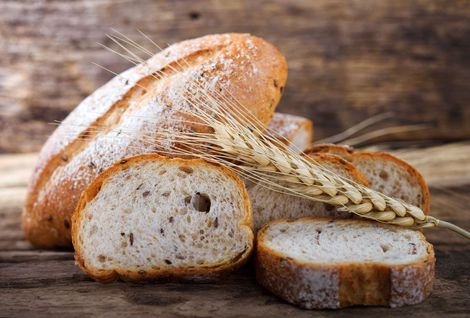 Ein Laib Brot und eine Weizenähre auf einem Holztisch.