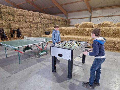 Zwei Jungen spielen Tischtennis und Tischfußball in einer Scheune voller Heuballen.