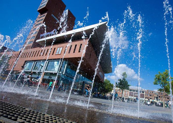 Vor einem Gebäude spritzt ein Brunnen Wasser.